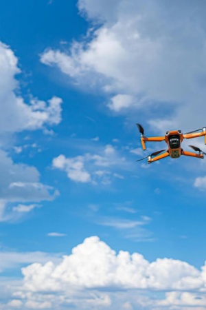 Imagem de um drone amarelo a voar no céu azul com algumas núvens